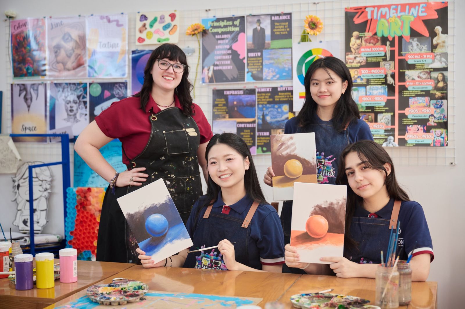 Art teacher with three students holding their painted sphere studies